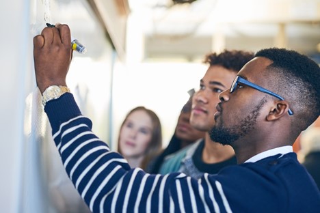 A man writes on a white board while others look on